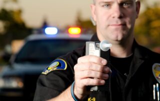 a police officer holds the breath test machine for a suspect to blow into with a police car in the background