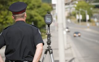 a north american policeman waits to catch speeding drivers with a radar gun. (shot with minimum depth of field. focus is on the police officer and radar gun.)