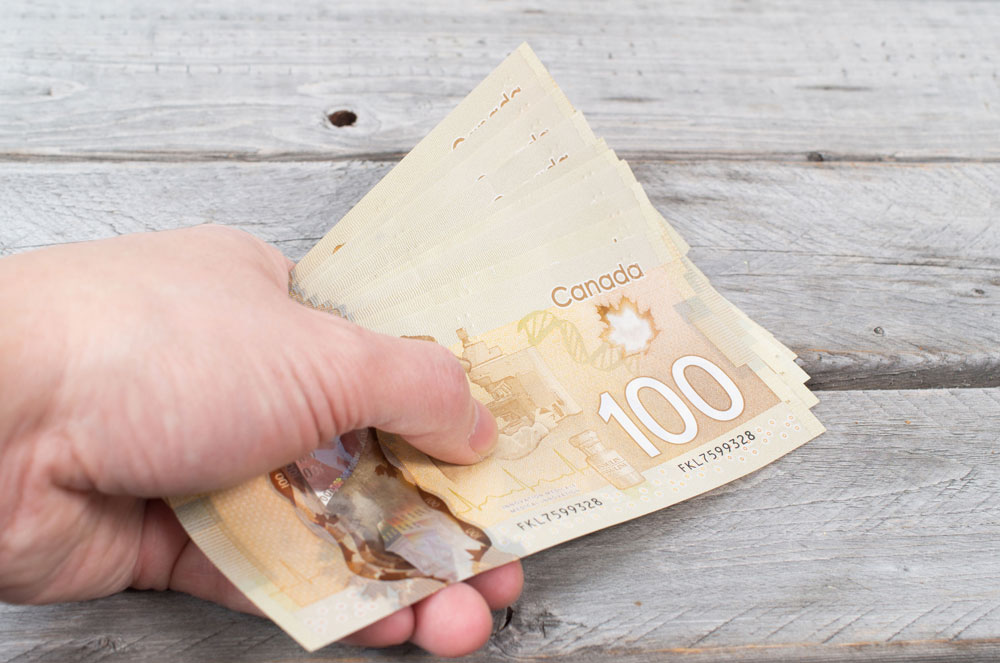 hand holding a bunch of brown bank notes on a wooden table